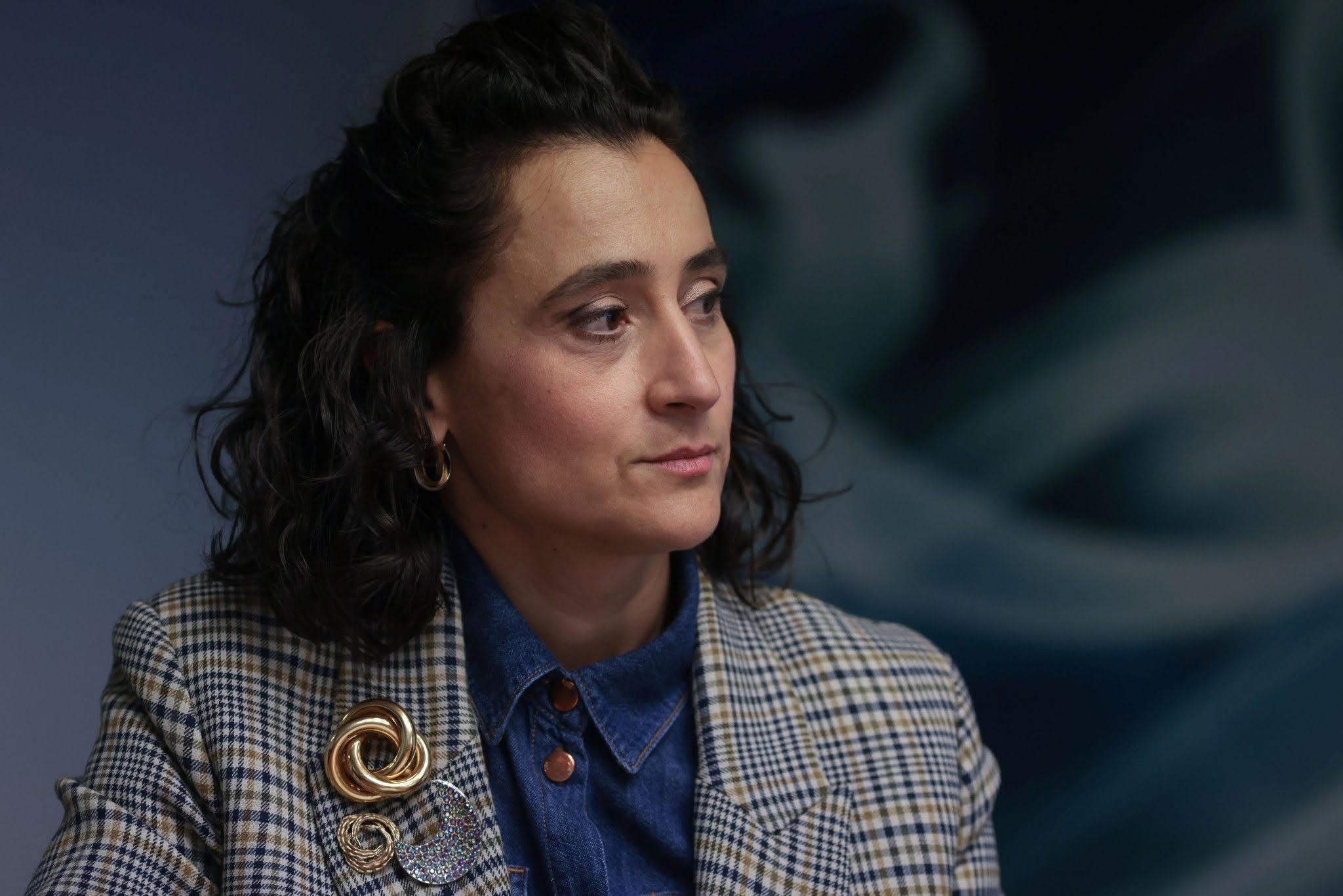 Ioana Ruxandra Victoria Ciocan, noul ministru al Culturii, &icirc;ntr-o cămașă de jeans, purt&acirc;nd pe deasupra un sacou &icirc;n carouri cu broșe de diferite dimensiuni &icirc;n piept.