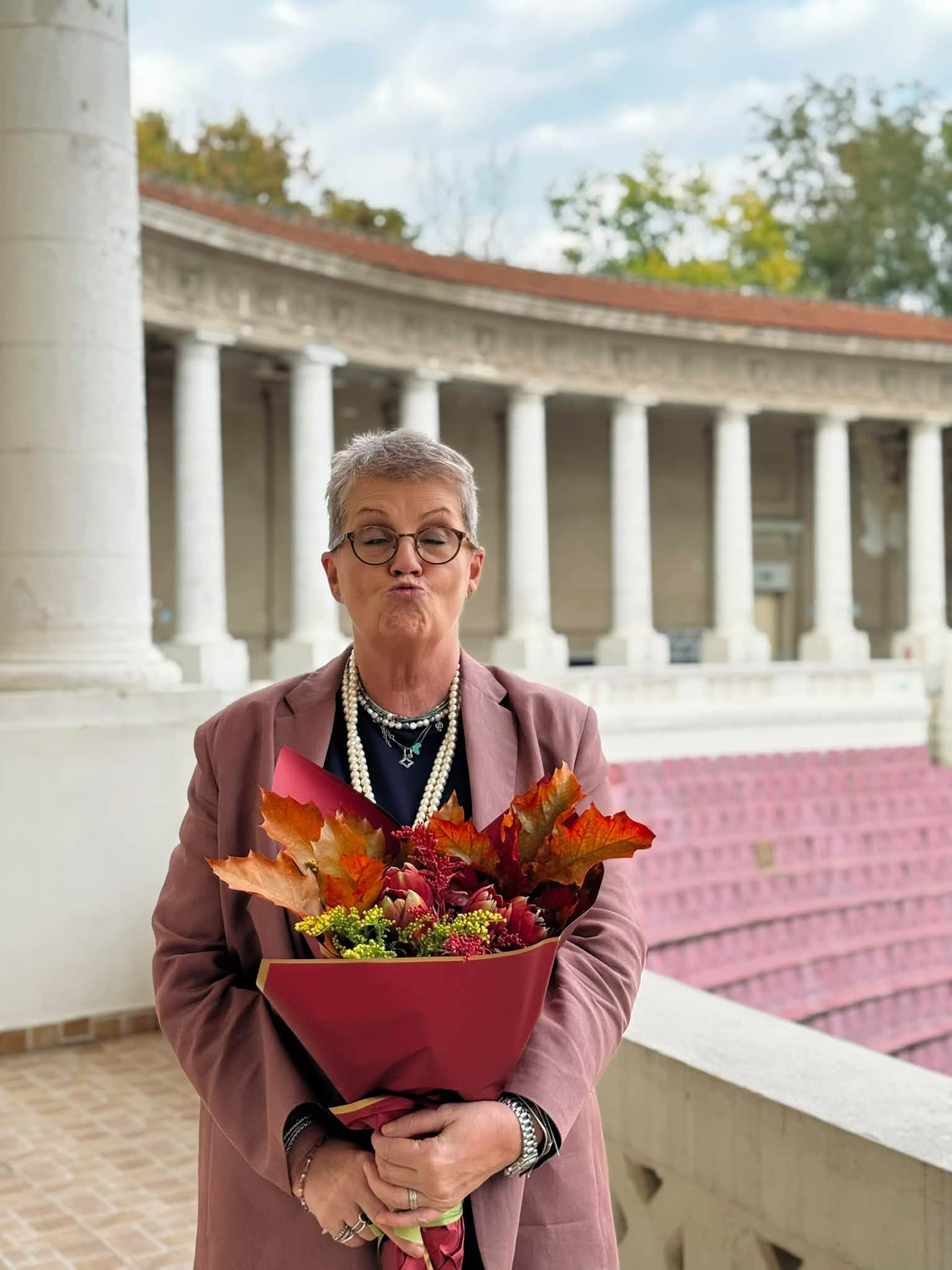 Crina Mardare la 68 de ani, țin&acirc;nd &icirc;n brațe un buchet de flori tomnatic, &icirc;n timp ce poartă foarte multe inele pe degete, brățări, un ceas și mai multe coliere la g&acirc;t, iar hainele e sunt asortate cu florile și frunzele din buchet