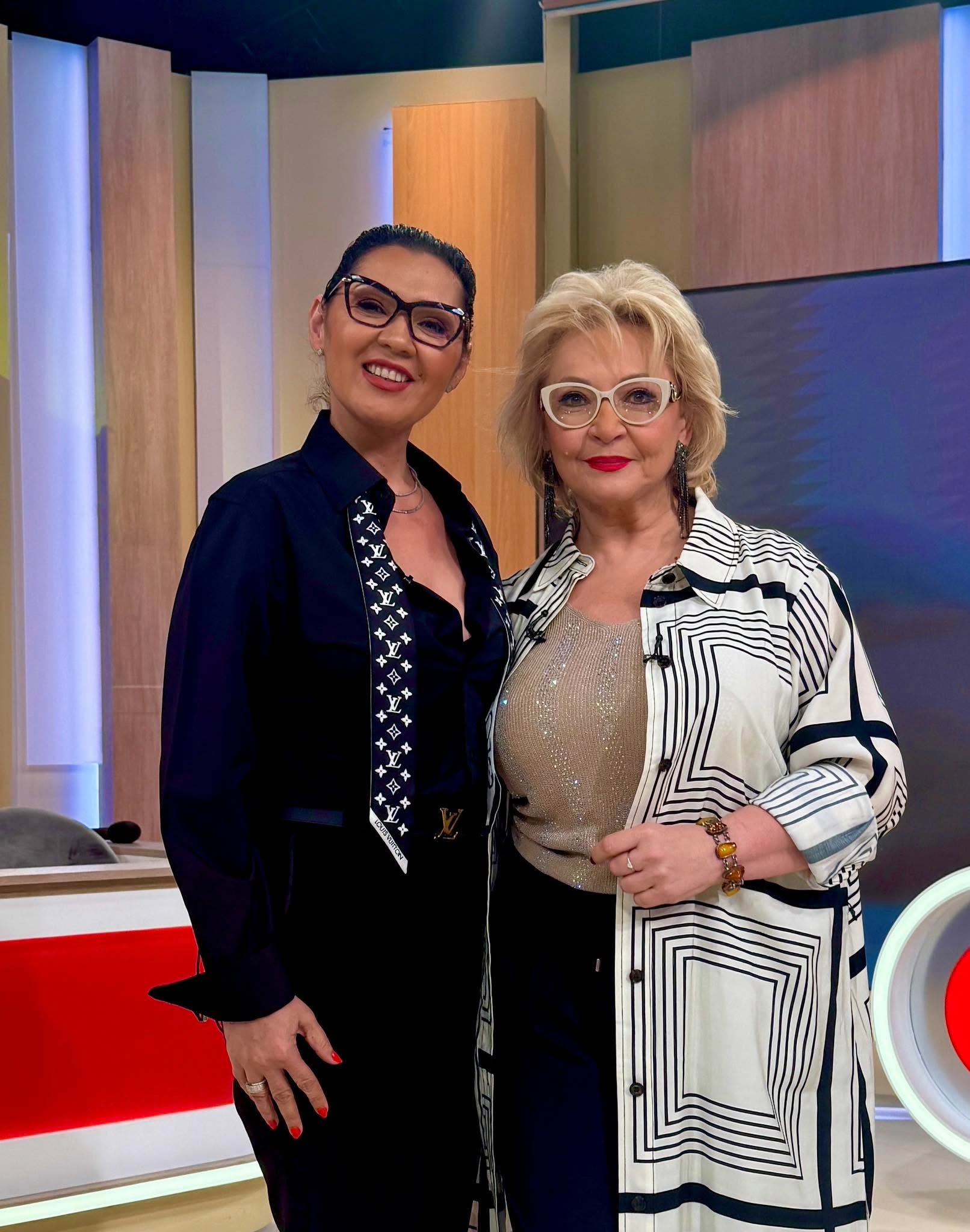 Minodora și Mihaela Tatu zâmbitoare în platoul unei emisiuni, în timp ce purtau amândouă ochelari de vedere și erau îmbrăcate în negru și alb