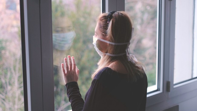 Femeie cu masca stand la geam