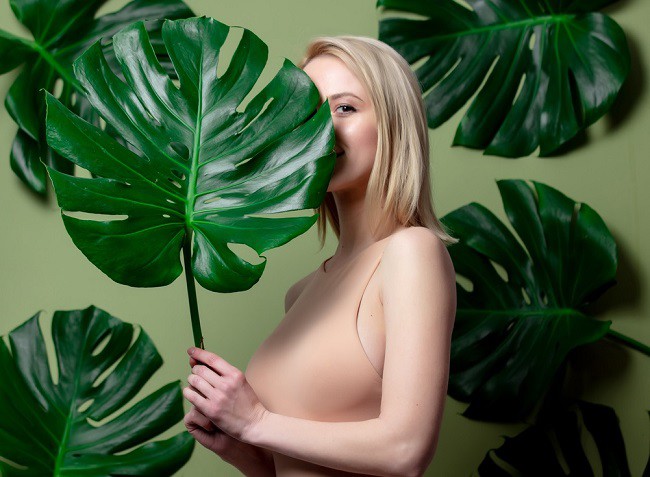 Tanara blonda in maiou nud, tinand in mana frunza de monstera deliciosa