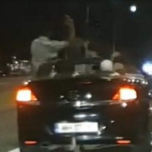 Momentul în care un şofer teribilist ia mâinile de pe volan şi se ridică in picioare, din decapotabilă